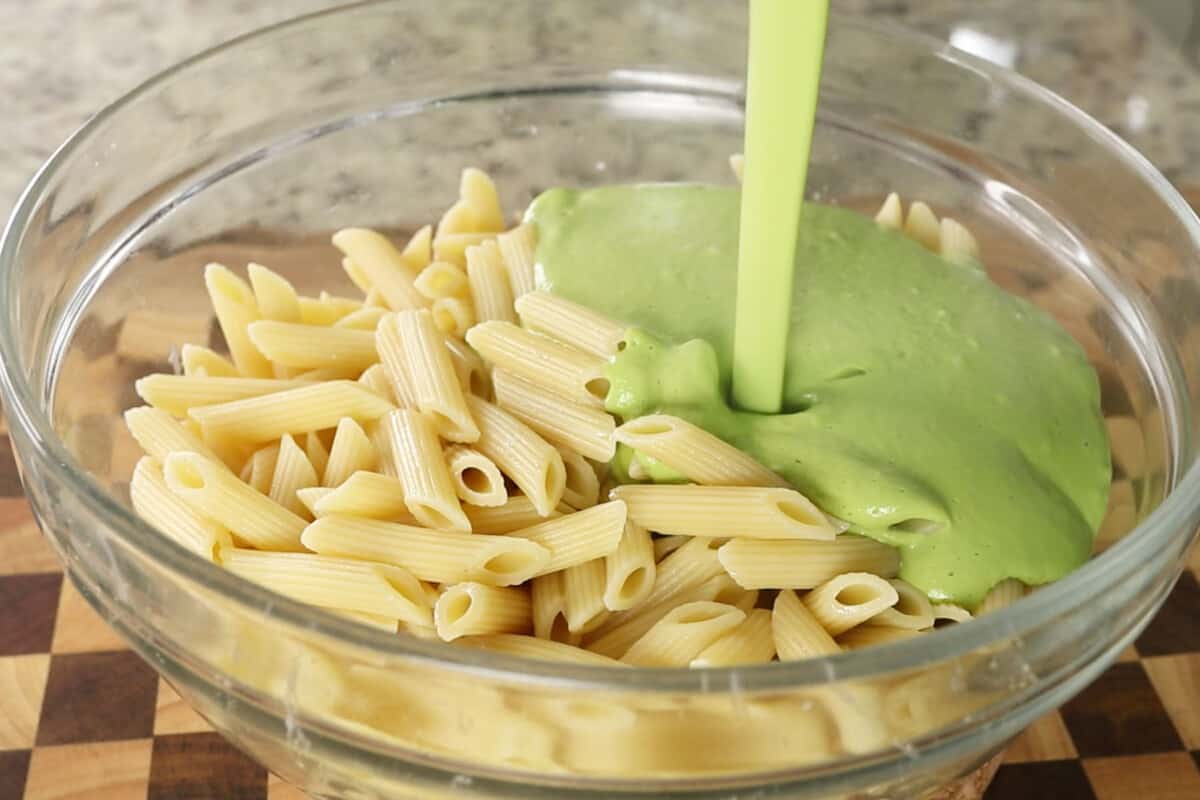 step by step: pouring creamy pea pesto sauce over cooked pasta in large glass bowl