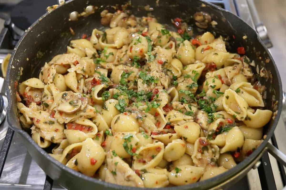 large pan full of cooked pasta with fresh basil and black pepper on top