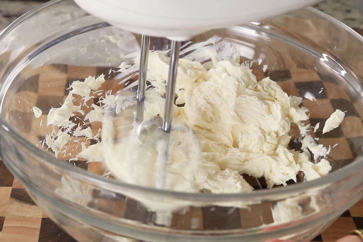 Step by step: Using a hand mixer to whip the butter cream frosting in a large glass bowl