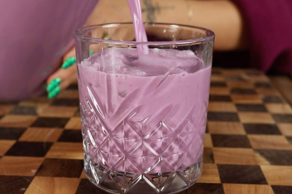 pouring ube horchata into glass cup with ice on checker board surface
