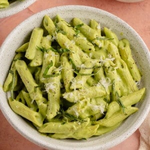 white bowl filled with pea pesto pasta stopped with fresh basil and parm on pink background