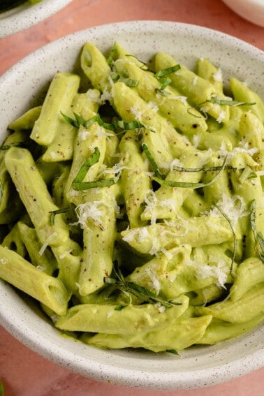 close up image of creamy pea pesto pasta topped with fresh basil and parm