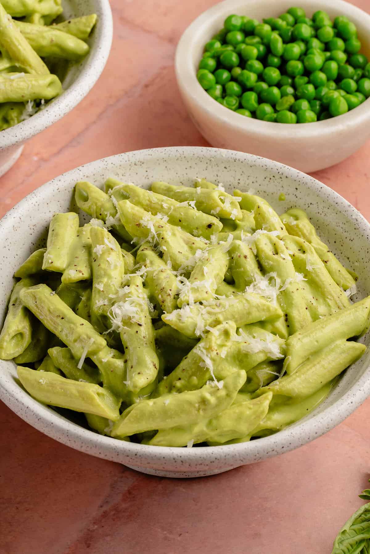 creamy pea pesto pasta in a bowl on a pink background with a side of peas