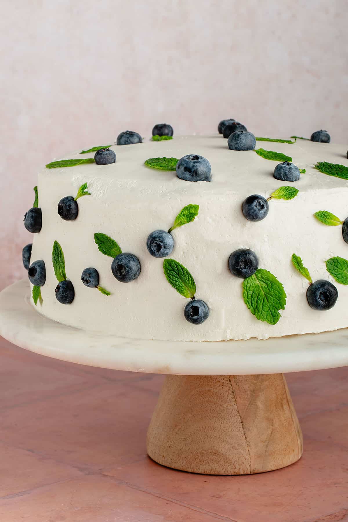 vegan vanilla cake with vanilla buttercream frosted decorated with blueberries and mint on a cake stand