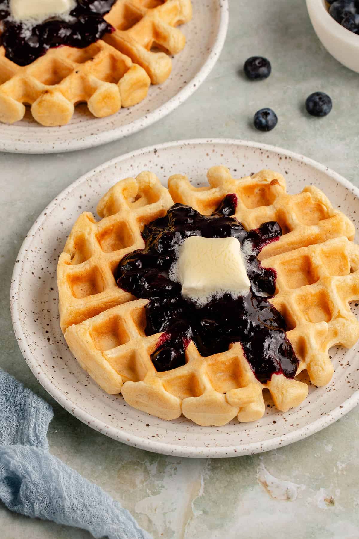 golden waffle on white plate with blueberry compote and melting pat of butter