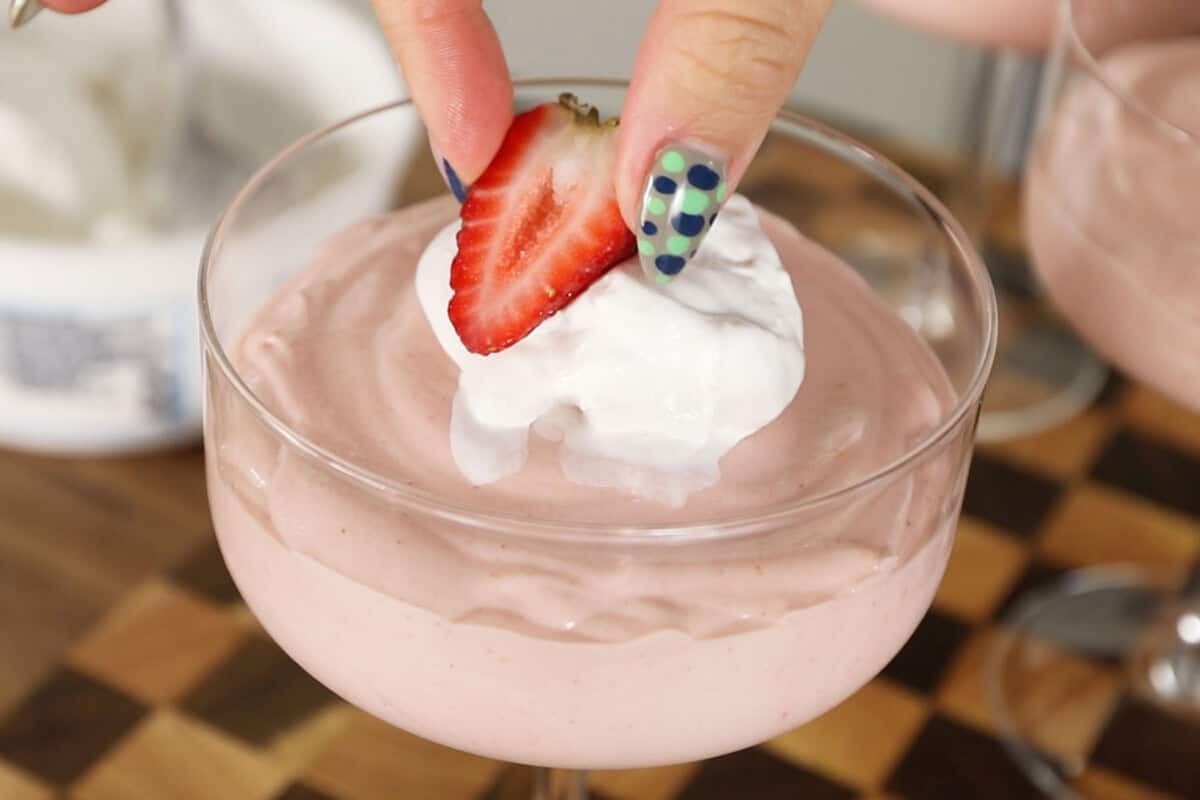 adding a fresh strawberry on top of strawberry mousse with whipped cream