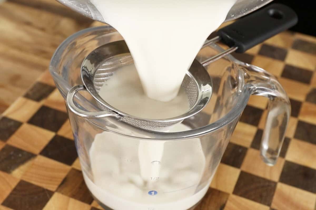 step by step - pouring evaporated milk through a strainer into a glass measuring cup