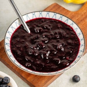 blueberry compote in small bowl with metal spoon on wooden board