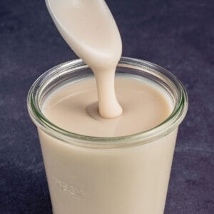a jar of vegan sweetened condensed milk with a spoon drizzling it down