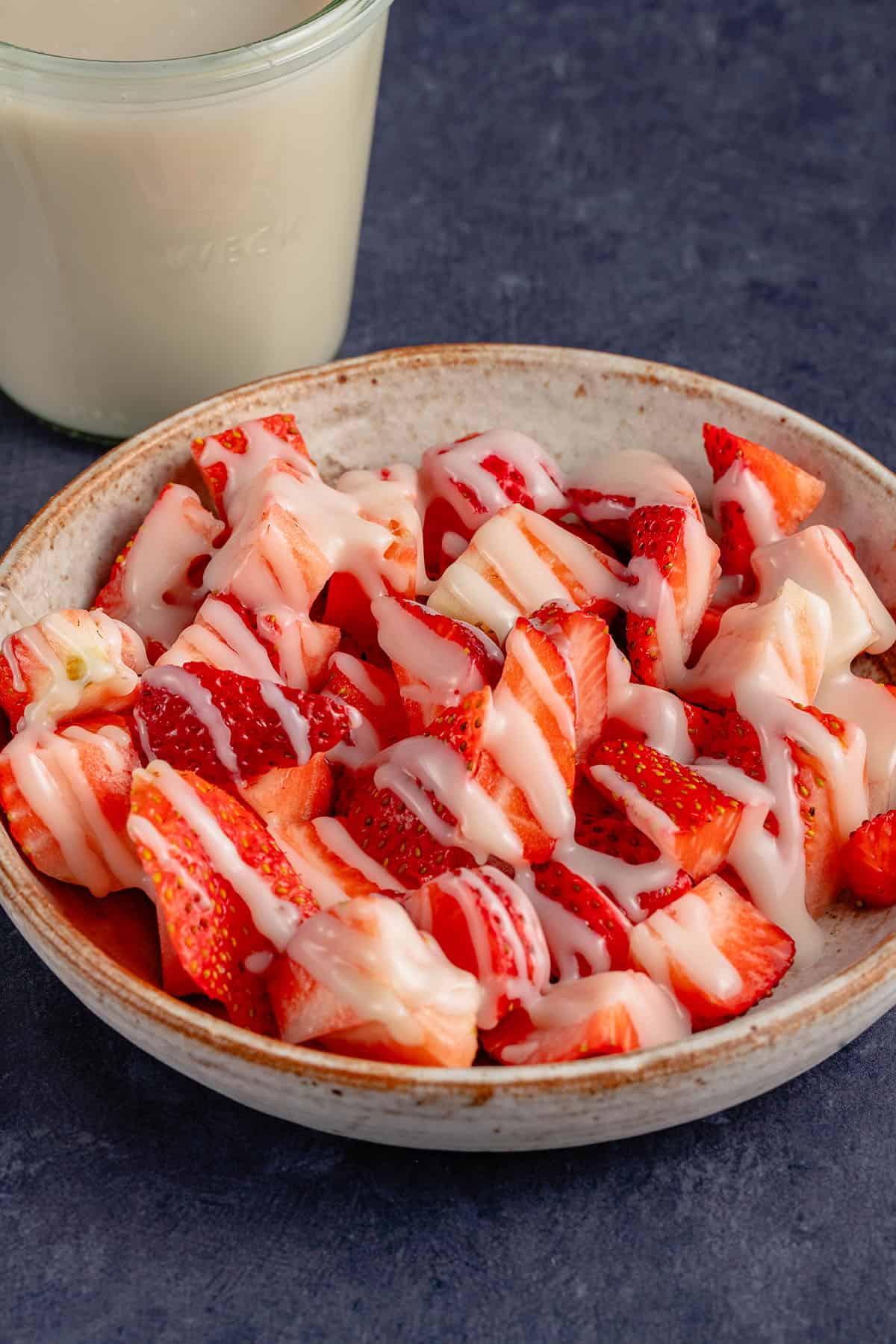 vegan condensed milk drizzled over strawberries in a bowl with a jar of condensed milk behind it.
