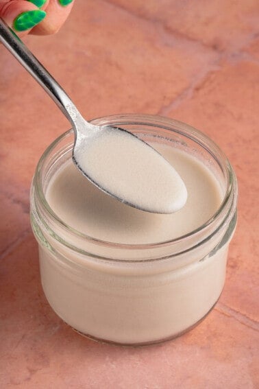 spoonful of vegan evaporated milk in short jar on pink tile backdrop