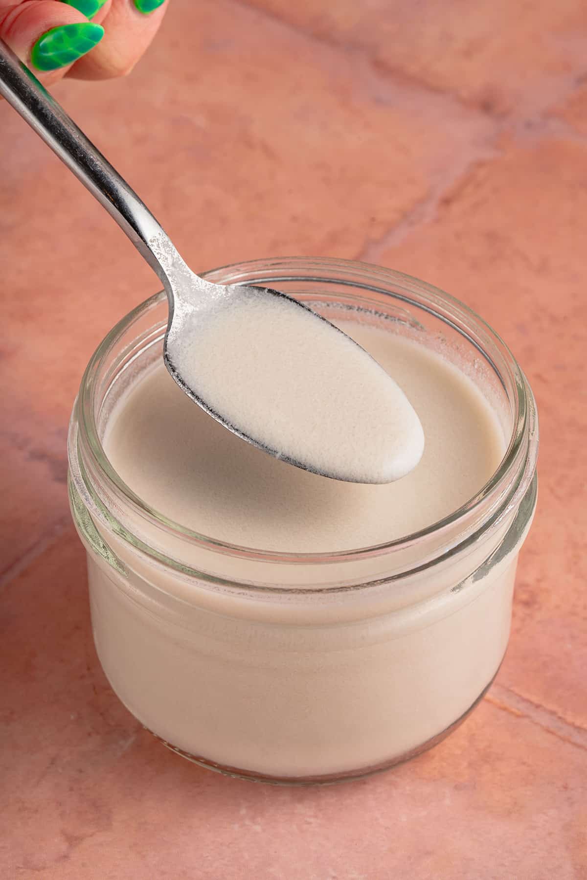 spoonful of vegan evaporated milk in short jar on pink tile backdrop