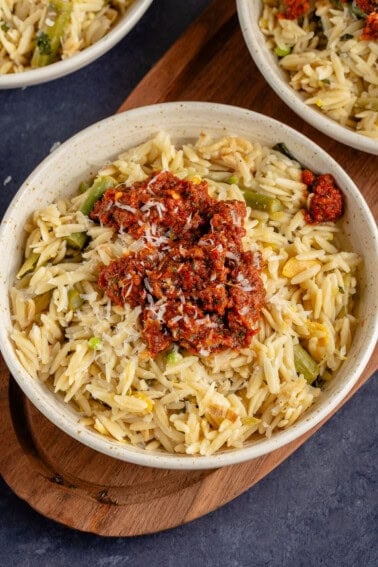 close up photo of spring orzotto in white bowl with sun dried tomato pesto