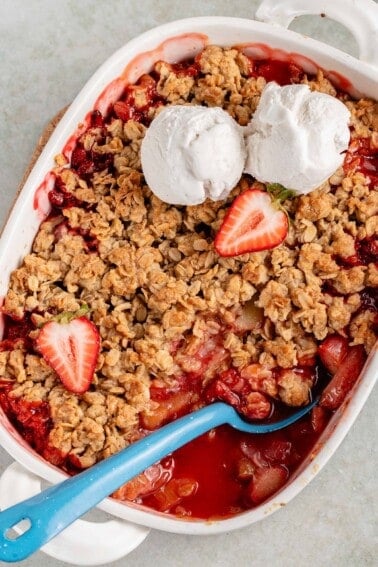 overhead ov strawberry rhubarb crisp in a white baking dish with blue spoon and ice cream