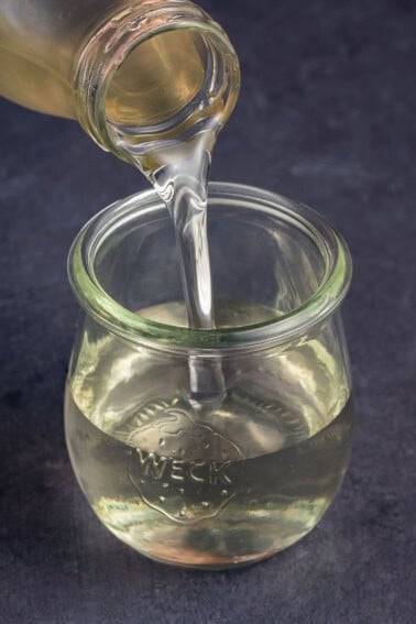 close up photo of pouring simple syrup in glass jar on blue backdrop