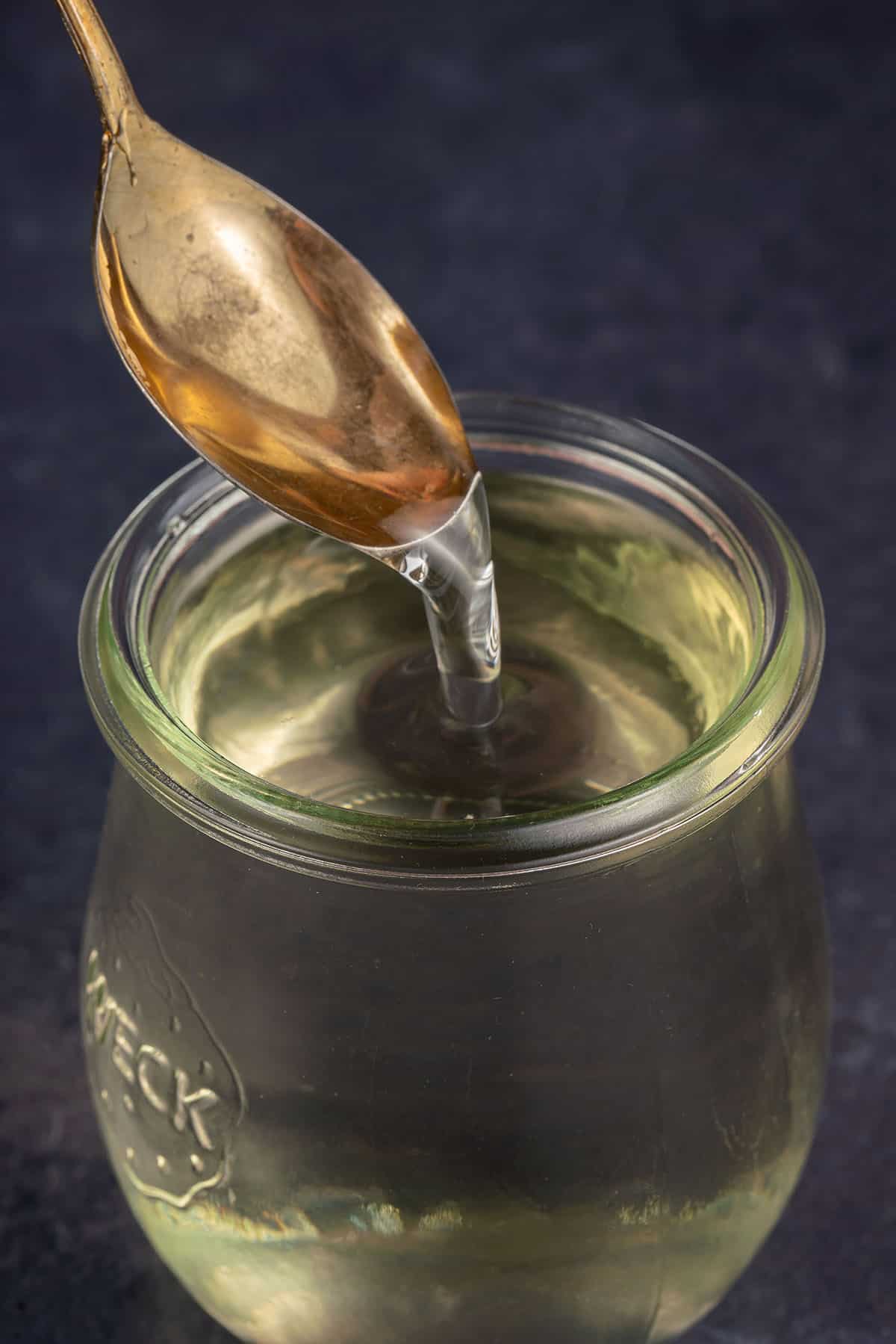 close up photo of spoon in simple syrup in glass jar on blue backdrop