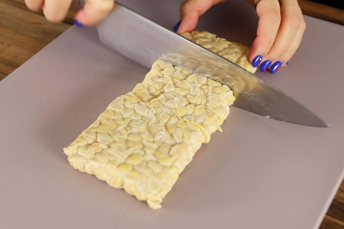 slicing uncooked tempeh on cutting board
