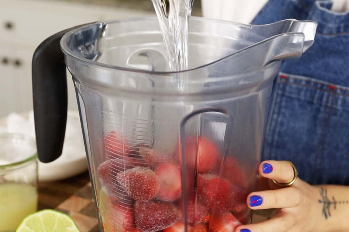 pouring run over frozen strawberries in a blender container