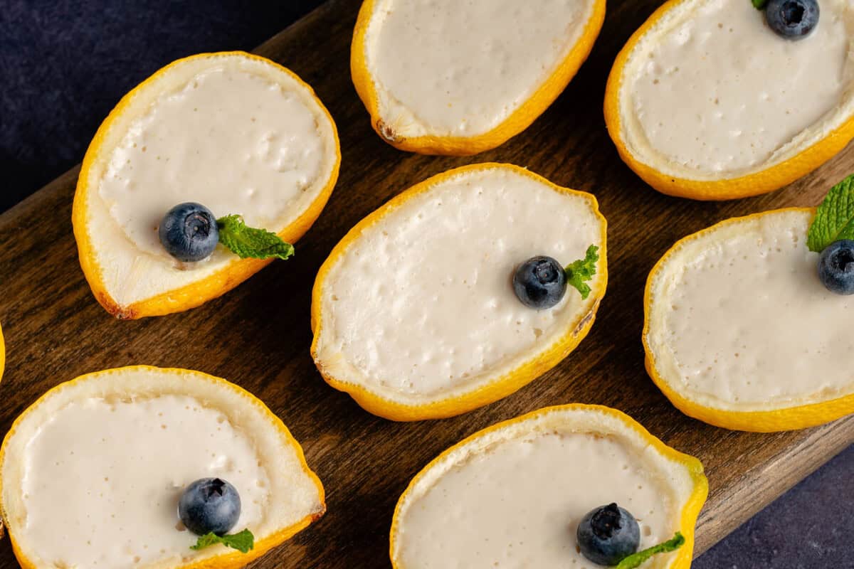 lemon peels filled with lemon posset on wooden board garnished with blueberries and mint