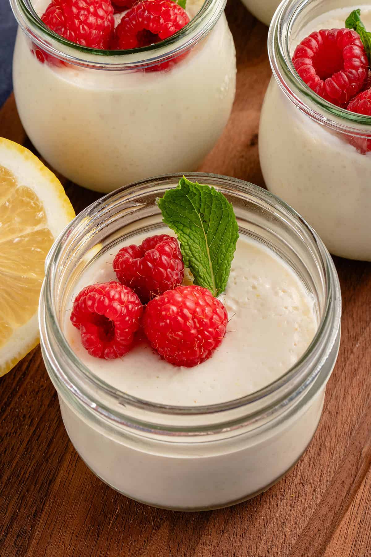 small jar of lemon posset with a garnish of raspberries and mint with a lemon peaking in