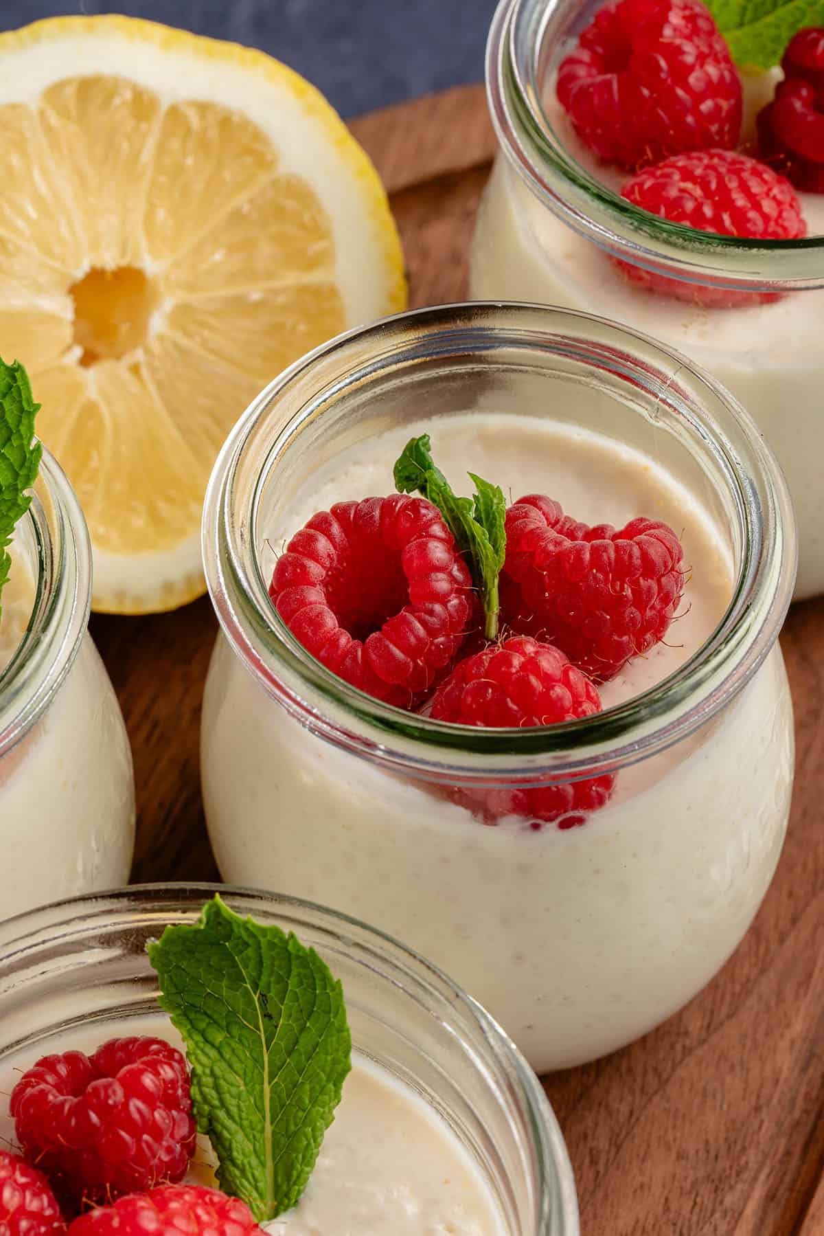 tulip jar filled with lemon posset topped with raspberries and mint with a lemon in the background