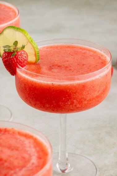 frozen strawberry daiquiri in a tall stemmed glass garnished with a strawberry and lime