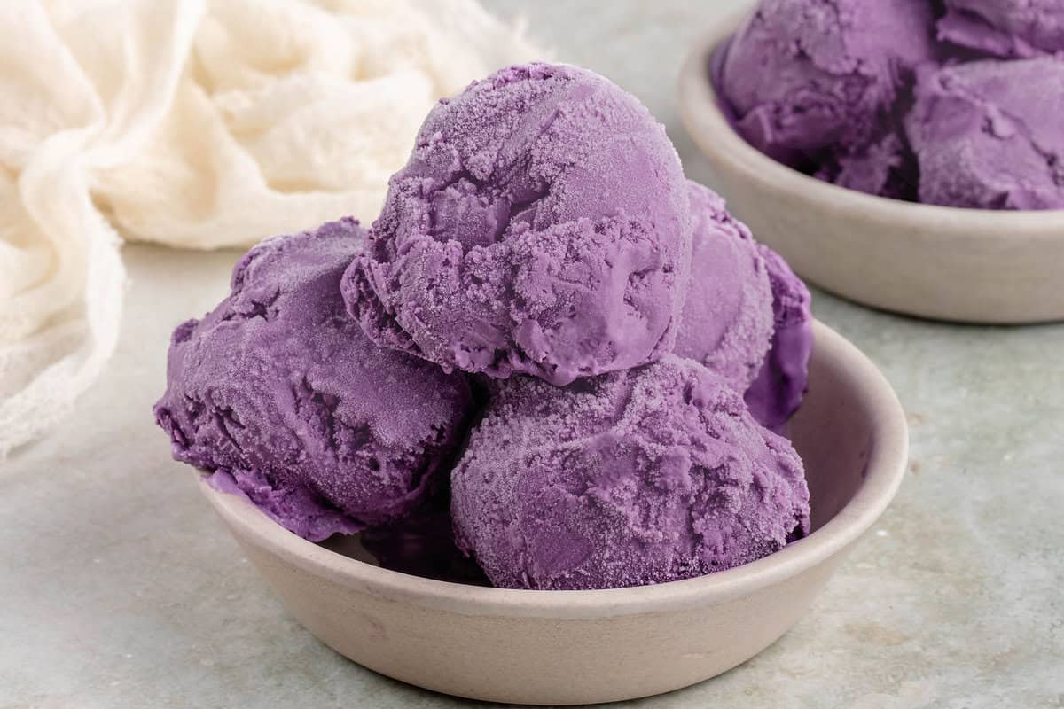 horizontal photo of vegan ube ice cream scoops in small gray bowls on white table