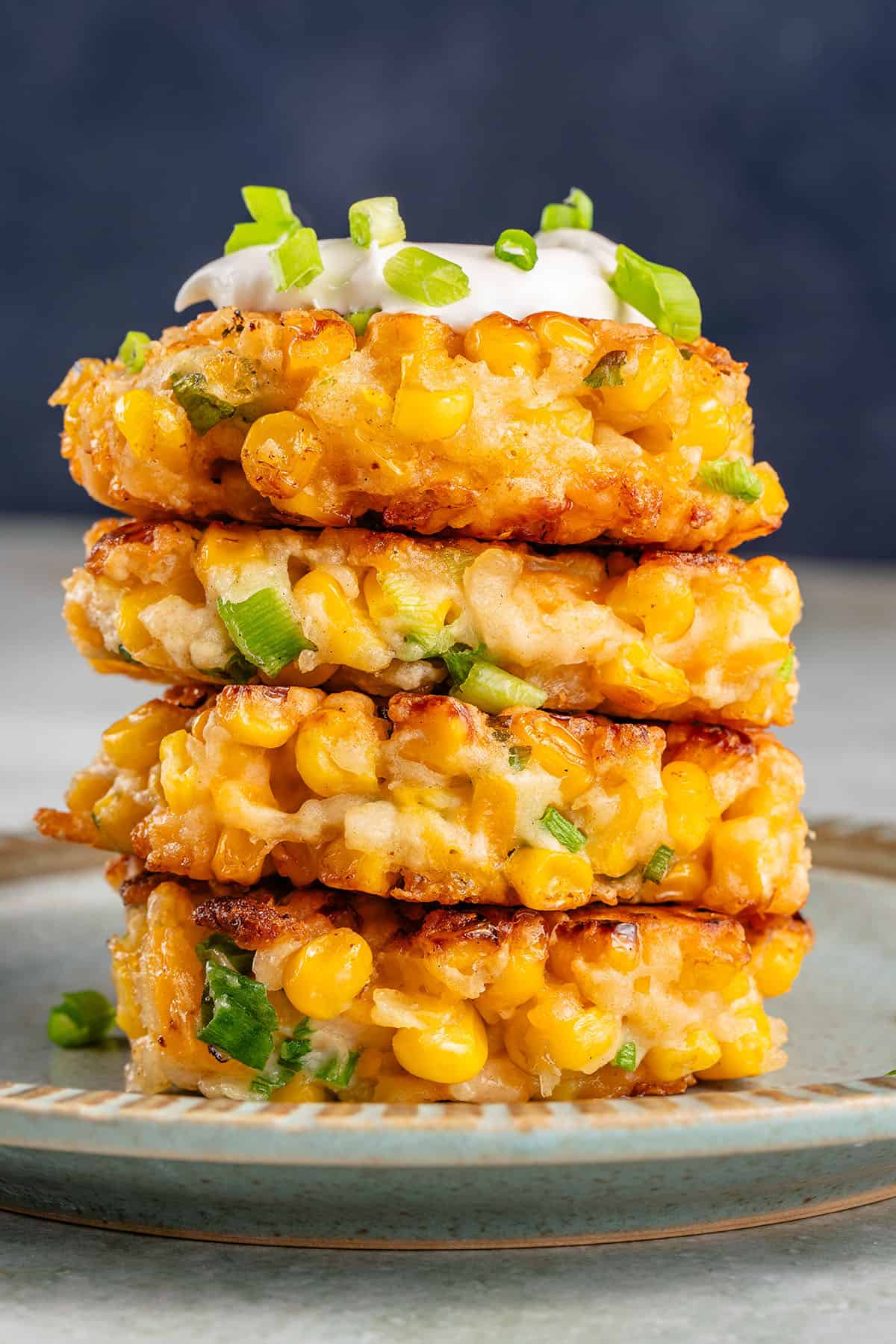 corn fritters in a stack on blue plate with mayo and scallions on top