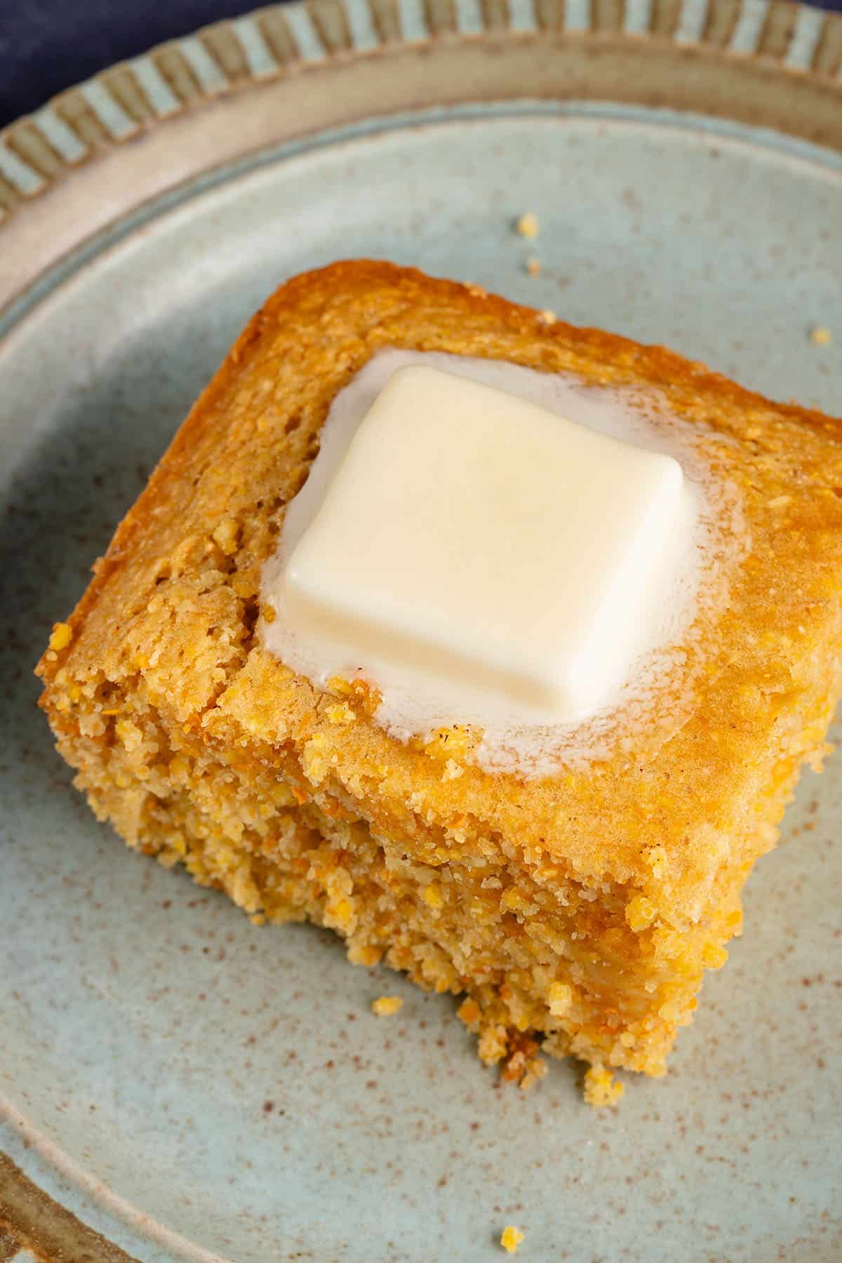 cornbread slice on a plate with a pat of butter melting on top