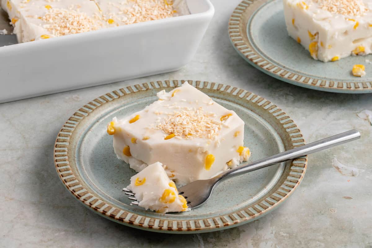 a slice of maja blanca topped with toasted coconut flakes on a blue plate with a fork holding a piece