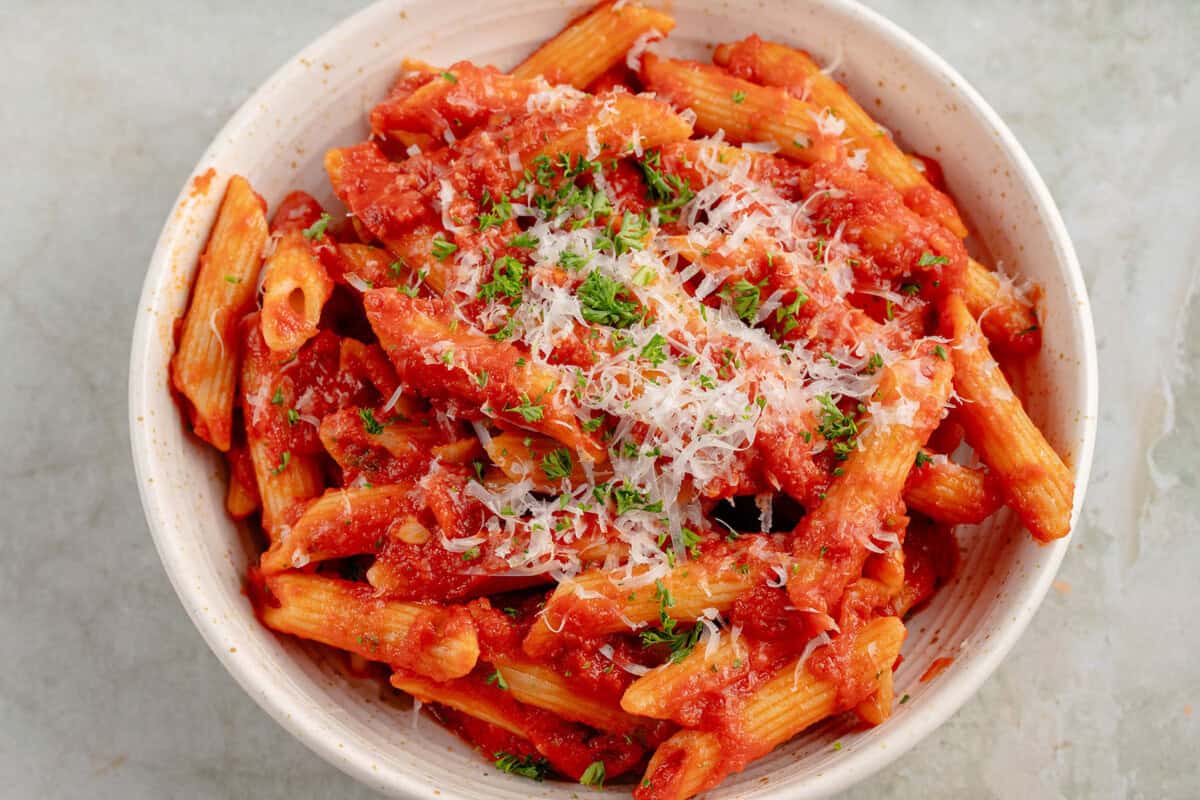 overhead photo of Penne All'Arrabbiata (Spicy Tomato Pasta) with vegan parmesan and parsley in white bowl