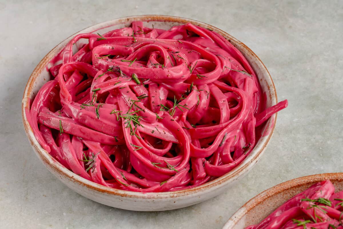 horizontal photo of bowl of creamy Vegan Beet Pasta sauce on fettuccine topped with dill