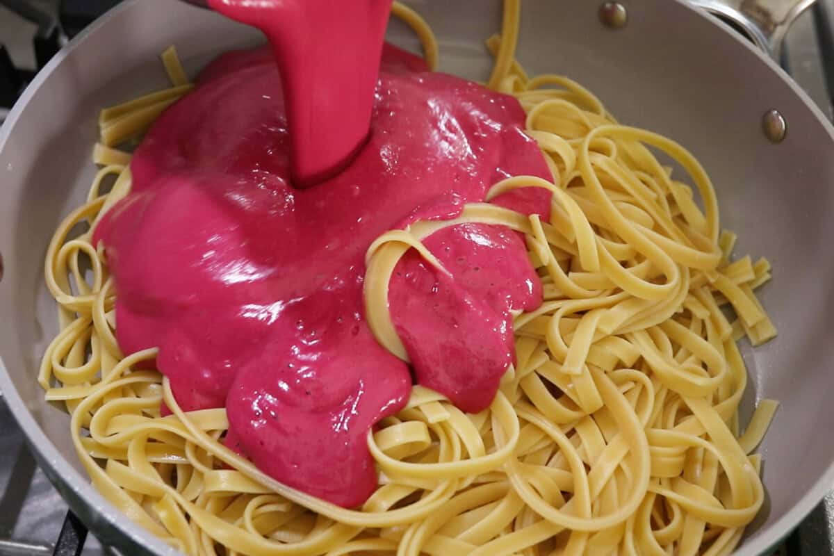 pouring bright pink beet pasta sauce over cooked fettuccine