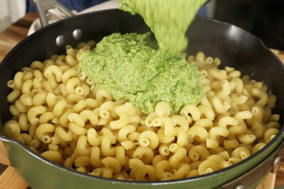 pouring zucchini pesto over cooked pasta noodles