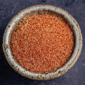 close up horizontal photo of a small bowl of homemade cajun seasoning on blue background