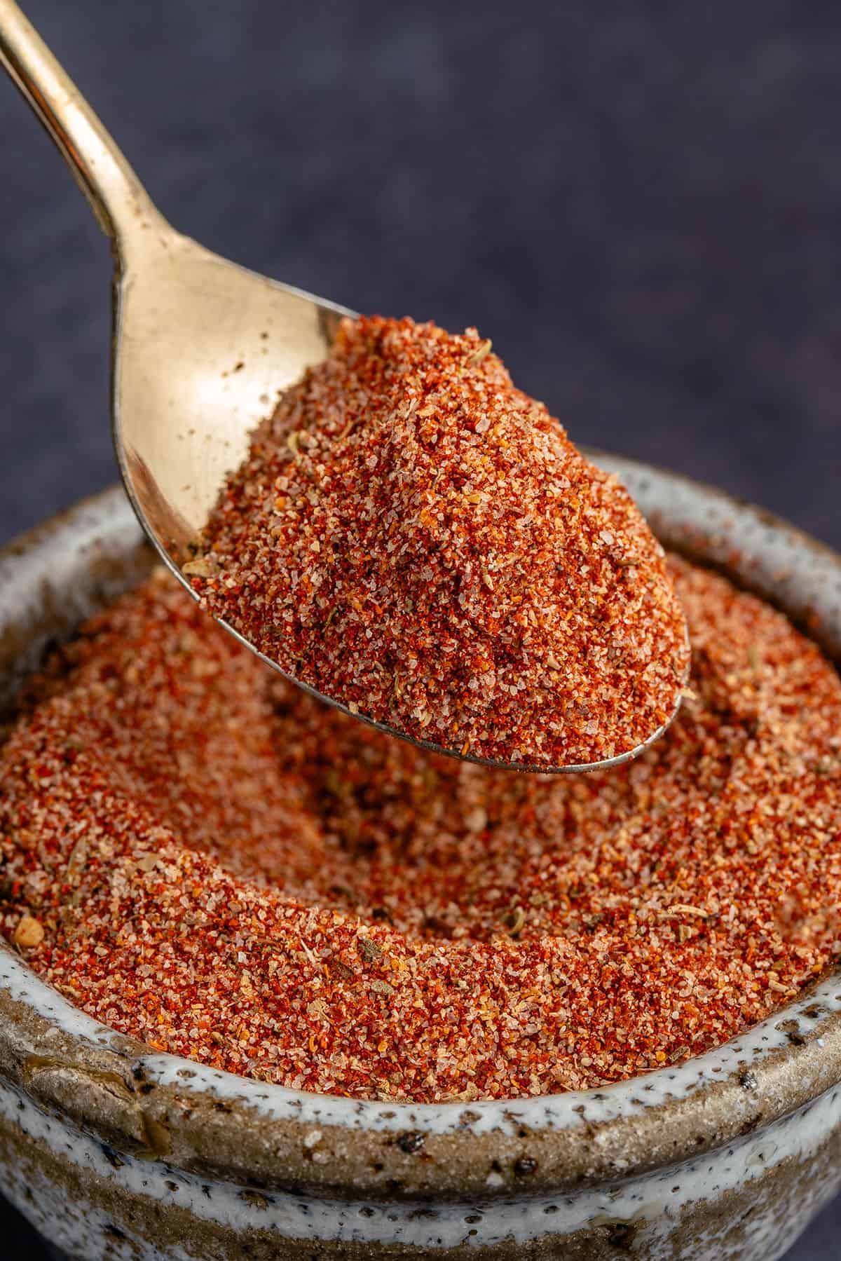 a gold spoon full of homemade cajun seasoning on blue background