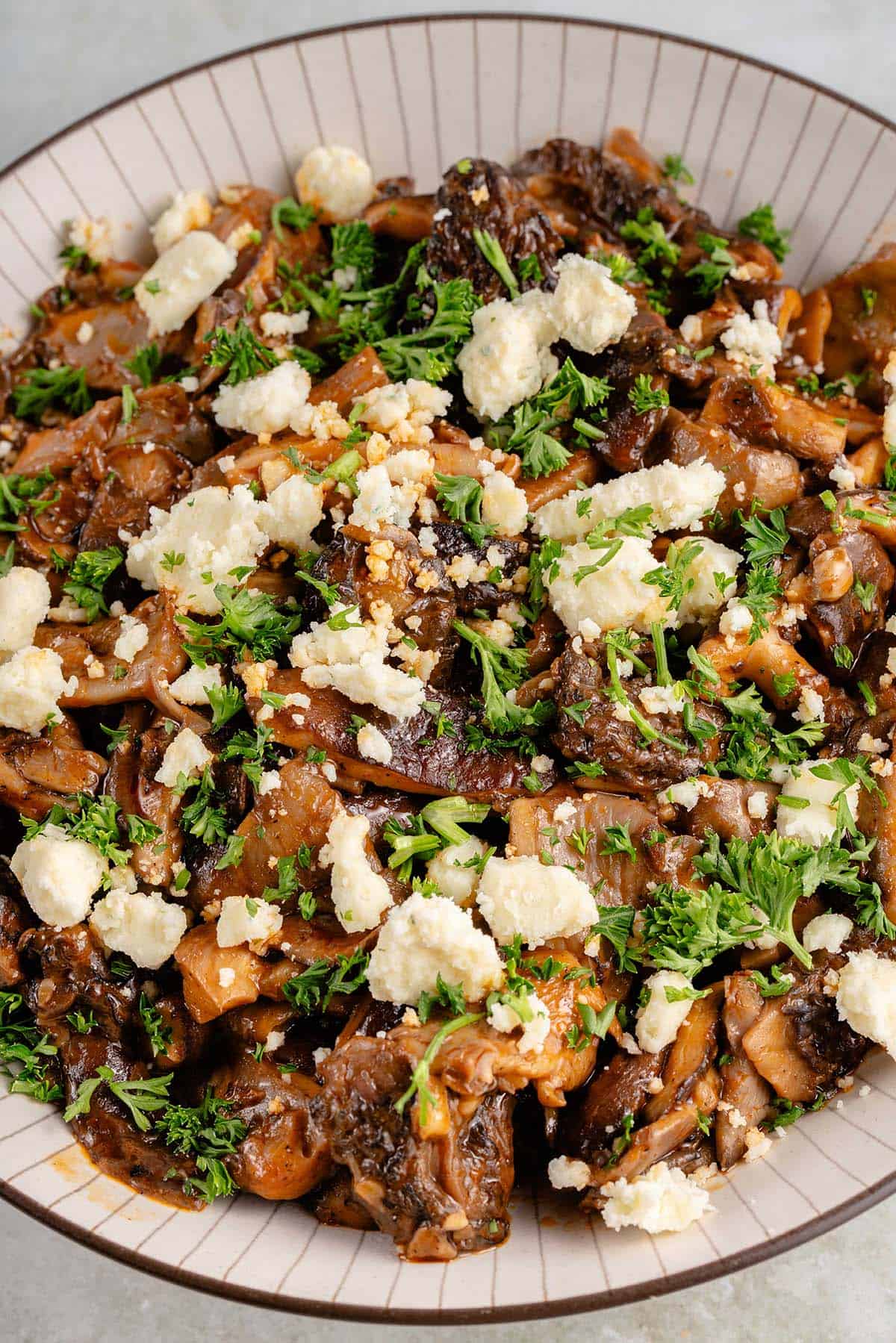 bowl of saucy buffalo mushrooms topped with parsley and vegan feta cheese crumbles