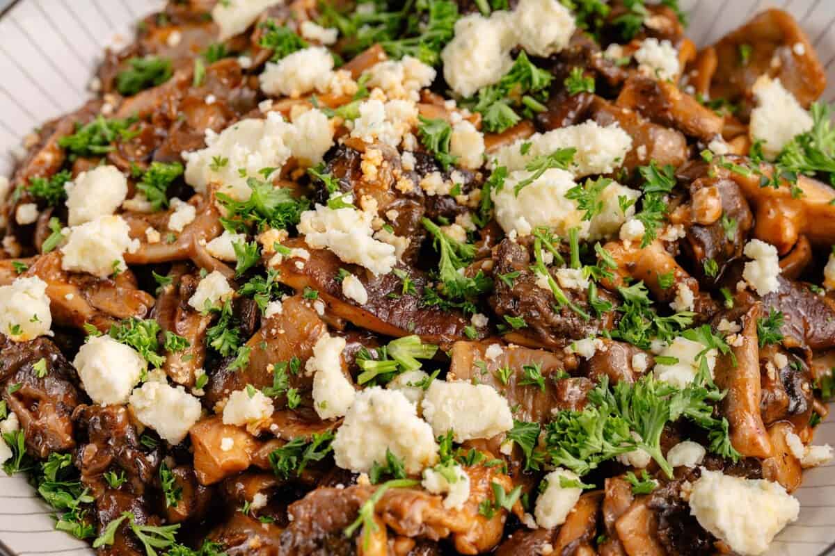 close up image of a bowl of saucy buffalo mushrooms topped with parsley and vegan feta cheese crumbles