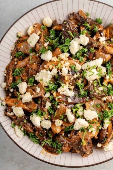 bowl of saucy buffalo mushrooms topped with parsley and vegan feta cheese crumbles