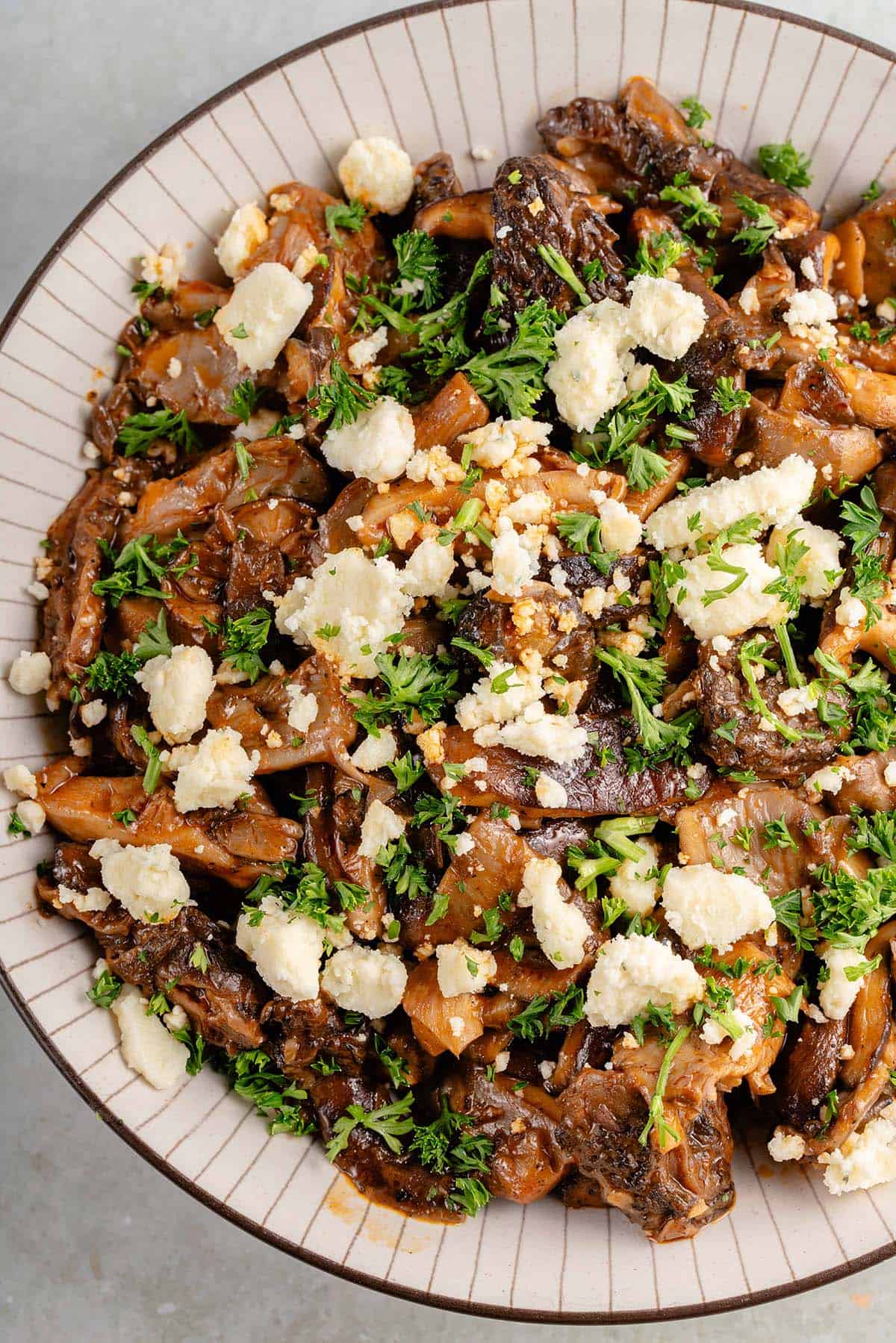 bowl of saucy buffalo mushrooms topped with parsley and vegan feta cheese crumbles