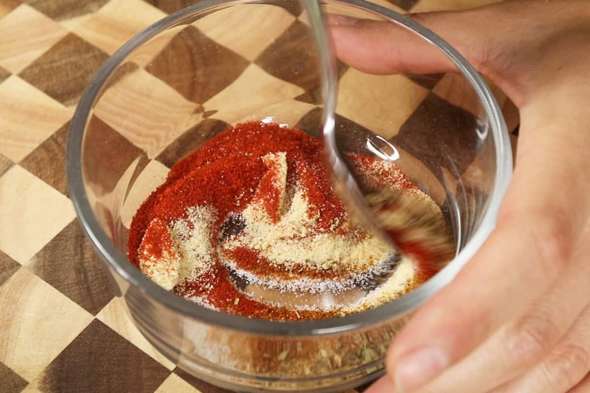 mixing together ingredients for homemade cajun seasoning in glass bowl