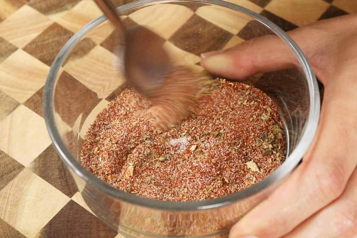 mixing together ingredients for homemade cajun seasoning in glass bowl