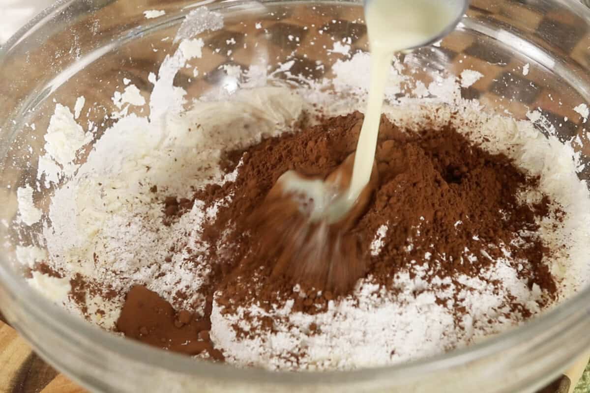 adding cocoa powder and milk to the bowl to make frosting