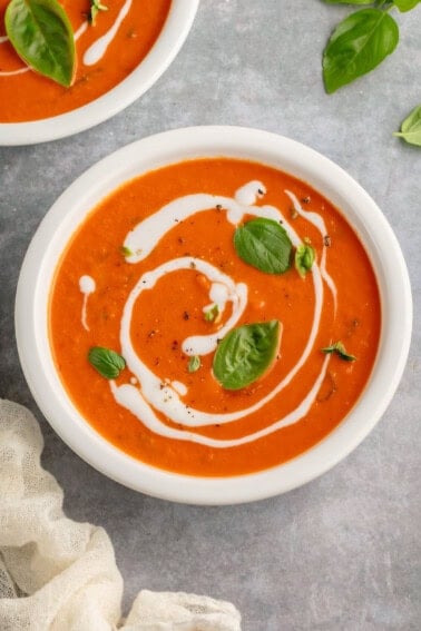 bowl of roasted red pepper tomato soup with a coconut milk drizzle and topped with fresh herbs and black pepper