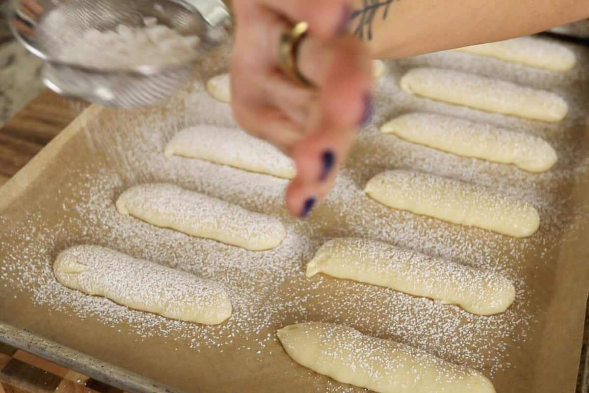 step by step: dusting ladyfinger cookie dough with powdered sugar