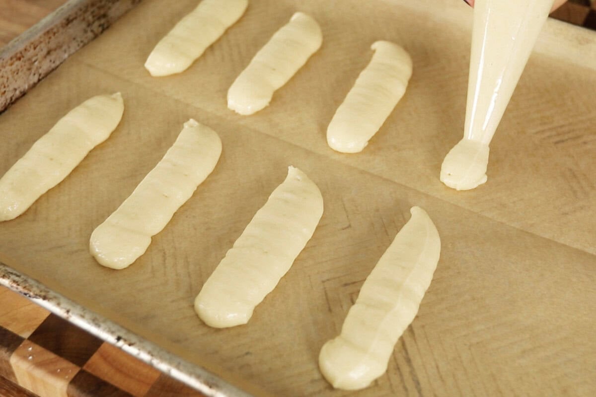 step by step: piping ladyfinger dough onto parchment lined baking sheet