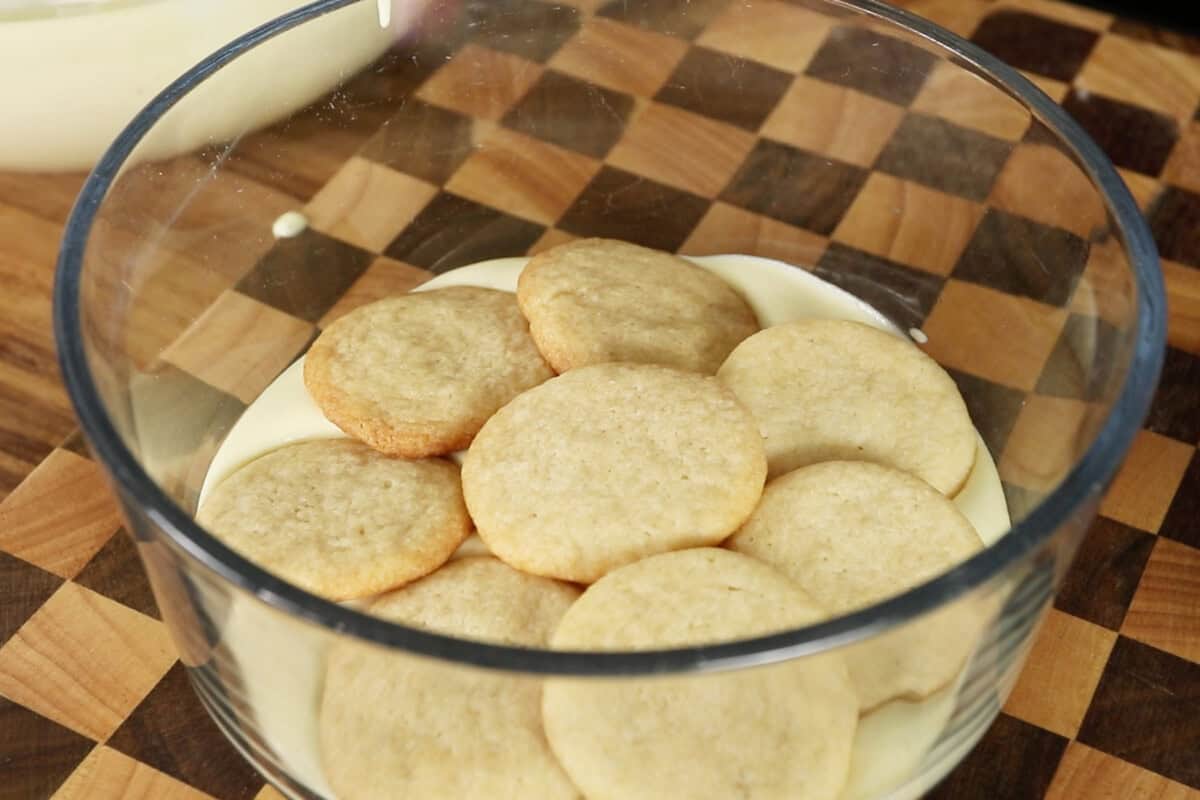 assembling vegan banana pudding with whipped cream in clear trifle dish