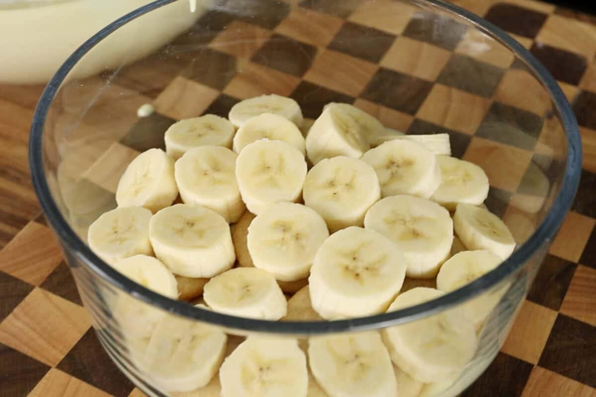 assembling vegan banana pudding with whipped cream in clear trifle dish