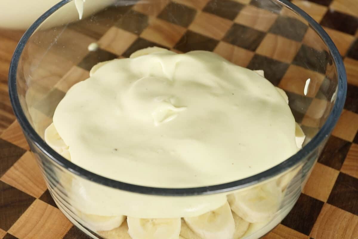 assembling vegan banana pudding with whipped cream in clear trifle dish