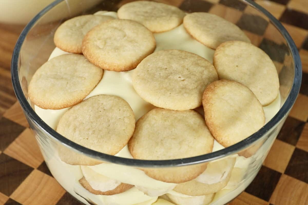 assembling vegan banana pudding with whipped cream in clear trifle dish